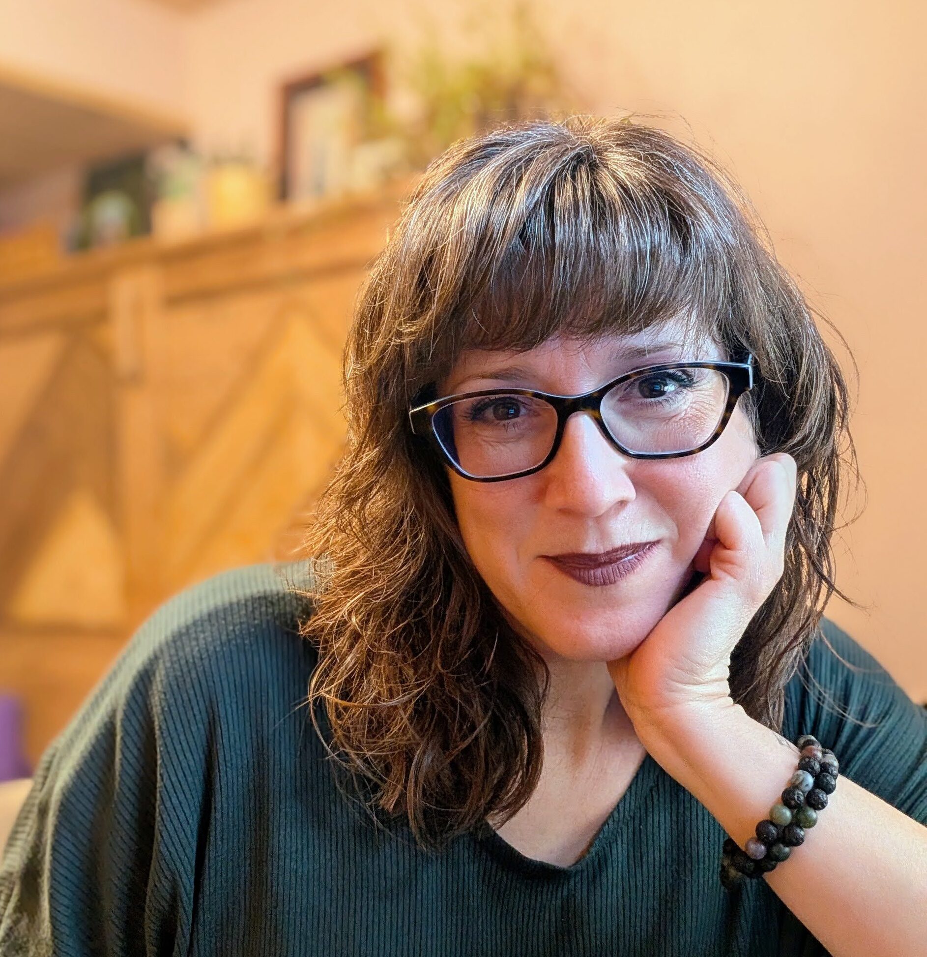 Me, leaning my cheek on my hand and staring into the camera with a small smile. My hair is loose and wavy, and I'm wearing dark brownish mauve lipstick.